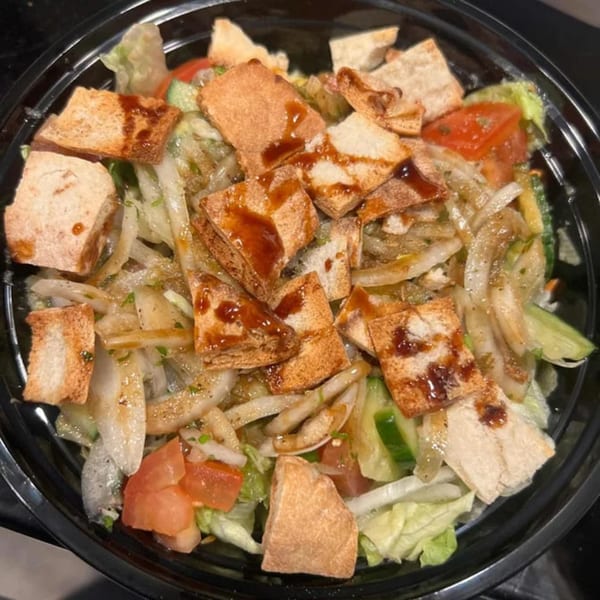 A close-up of Hala's Grill's Fattoush salad with lettuce, tomatoes, cucumbers, onions, and pita bread.