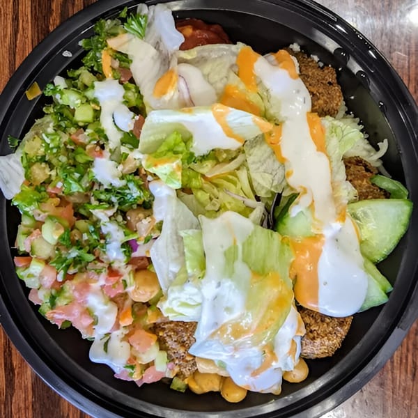 A Hala's Grill halal bowl with falafel, salad, and two sauces in a black bowl.