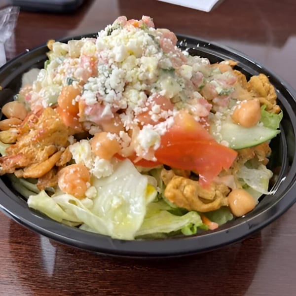 A Hala's Grill salad with lettuce, tomatoes, chickpeas, chicken, and feta cheese in a black bowl.