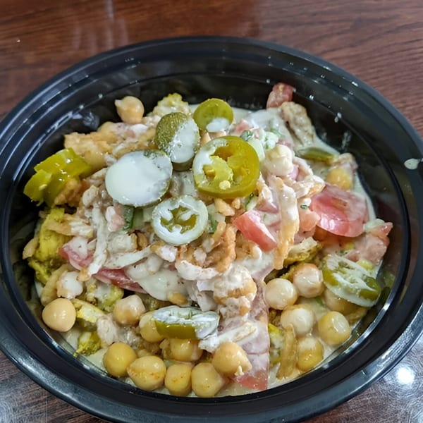 Hala's Grill halal bowl with chickpeas, tomatoes, jalapeños, and creamy sauce in a black container.