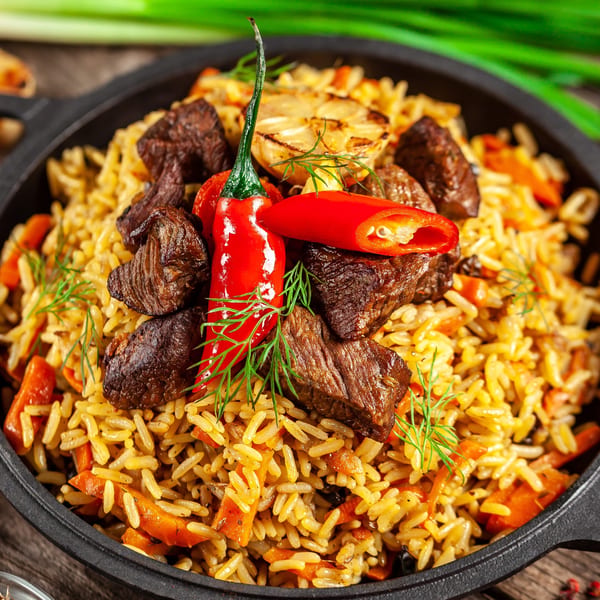 Halal pilaf with tender beef, carrots, and red chilies in a black skillet.