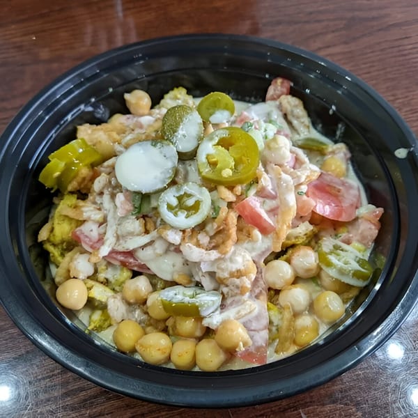 A Hala's Grill halal bowl with chickpeas, tomatoes, jalapeños, and white sauce.
